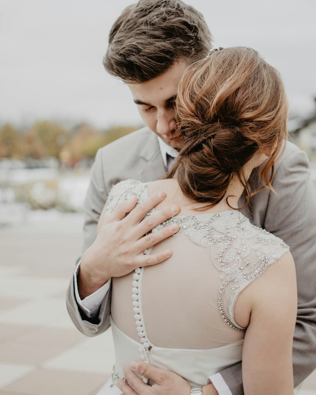 A couple in wedding attire holding each other close, photographed in soft daylight.